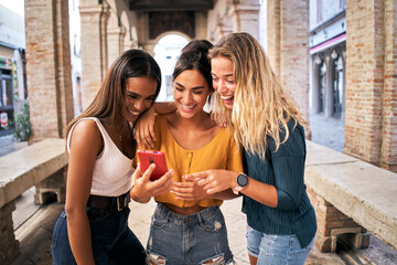 Three multiracial women using mobile phone outdoors. Youth and social media networking. 