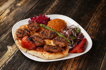 Turkish meatballs traditional kofte with onions, bulghur, roasted green pepper, and roasted tomato on a white plate. Delicious Turkish kebab kofte. Spicy meatballs kebab. 