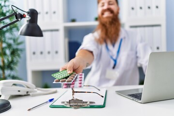 Young redhead man wearing doctor uniform prescribe pills at clinic