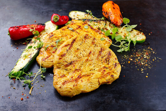 Traditionelle Putenschnitzel vom Grill in Curry Marinade mit gegrilltem Gem&uuml;se serviert als close-up auf einem alten rustikalen Board