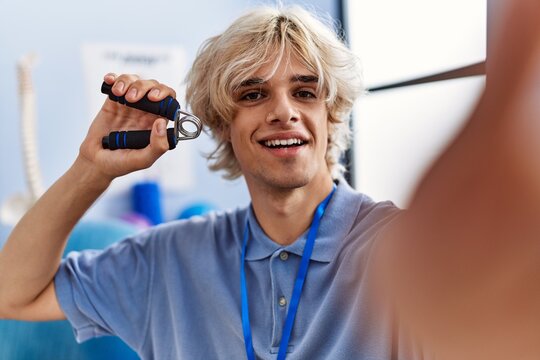 Young blond man pysiotherapist press hand making selfie by camera at rehab clinic