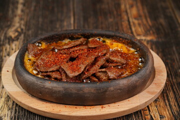 Delicious Fried eggs with pastrami inside in a casserole on wooden background. Fried eggs with pastrami made with butter.