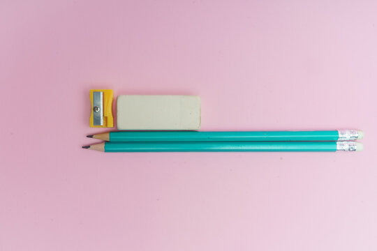 L&aacute;pices azules, borrador blanco y sacapuntas amarillo sobre fondo rosa.