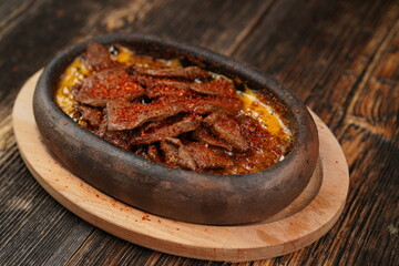 Delicious Fried eggs with pastrami and chilli pepper inside in a casserole on wooden background. Fried eggs with pastrami made with butter. 