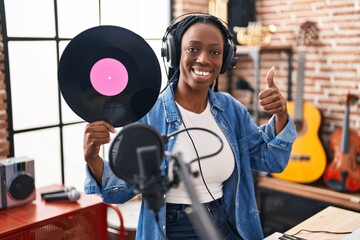 Beautiful black woman holding vinyl record at music studio smiling happy and positive, thumb up doing excellent and approval sign