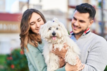 Man and woman holding dog hugging each other at park