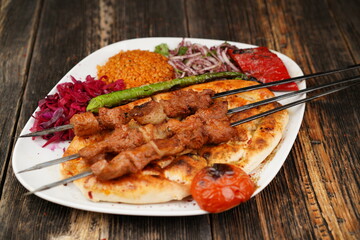 Beef shish kebabs with onion, rice, and tomatoes in a white bowl on wooden background. Traditionally marinated beef shish kebab. Traditional grilled kebabs.
