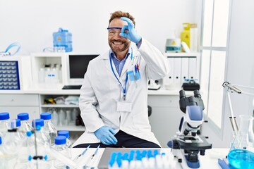 Fototapeta premium Middle age man working at scientist laboratory smiling happy doing ok sign with hand on eye looking through fingers