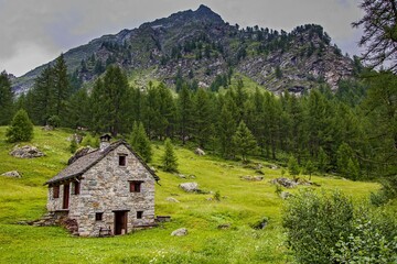 Fototapeta na wymiar Stone cottage on green meadow in Alpe Devero, Lepontine Alps, Ossola, Piedmont, Italy