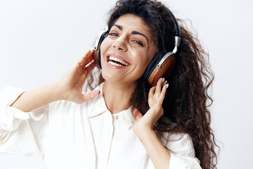 Portrait Overjoyed Happy Curly Beautiful Latin Woman Listening Cool Song In Headphones Singing Looks At Camera Isolated At White Studio Wall Background. Music Devices DJ Technology Huge Sale Concept