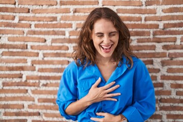 Beautiful brunette woman standing over bricks wall smiling and laughing hard out loud because funny crazy joke with hands on body.