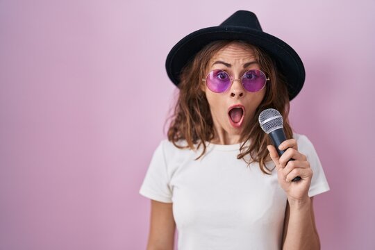 Beautiful brunette woman singing song using microphone scared and amazed with open mouth for surprise, disbelief face