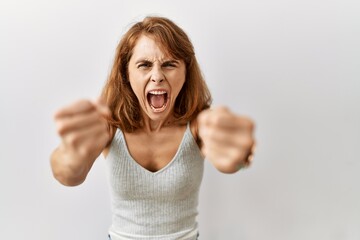 Beautiful caucasian woman standing over isolated background angry and mad raising fists frustrated...