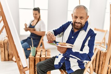 Obraz premium Young artist woman and senior painter man at art studio classroom painting on canvas with brush and oil painting