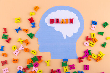 Word brain written by small colorful letters in head of paper human face lay on light pink background. Top view, flat lay