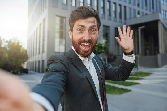 Happy businessman in suit make a selfie on background of his office building