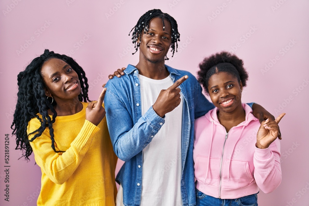 Poster Group of three young black people standing together over pink background with a big smile on face, pointing with hand finger to the side looking at the camera.