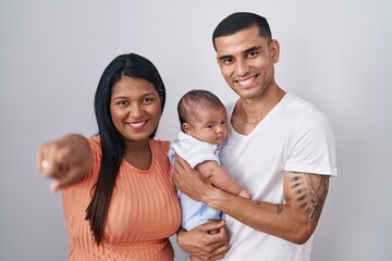 Young hispanic couple with baby standing together over isolated background pointing to you and the camera with fingers, smiling positive and cheerful
