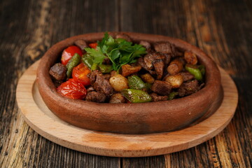 Title: Saute meat in a stew on a wooden background. Meat saute made with beef, mushroom, onion, green pepper and tomatoes. A delicious traditional Turkish food name is Guvec.