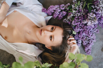 a sexy topless blonde in a white shirt on the floor with lilac flowers - obrazy, fototapety, plakaty