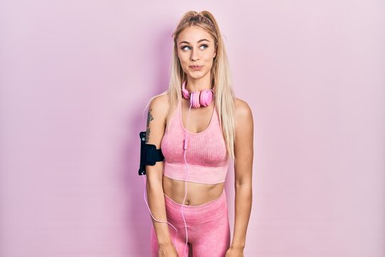 Young beautiful caucasian woman wearing gym clothes and using headphones smiling looking to the side and staring away thinking.