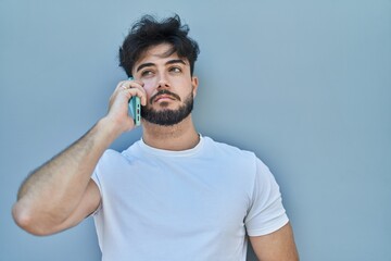 Young hispanic man talking on the smartphone over white isolated background