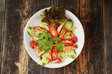 Salad with fried chicken. Salad made with fried chicken, tomatoes, cucumber, green pepper, and grated cheese in a white bowl. Delicious health food.