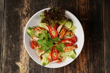 Salad with fried chicken. Salad made with fried chicken, tomatoes, cucumber, green pepper, and grated cheese in a white bowl. Delicious health food.
