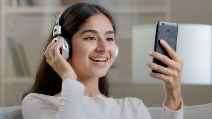 Joyful artistic arabic woman teenager wears headphones earphones listen music melodies choose audio...