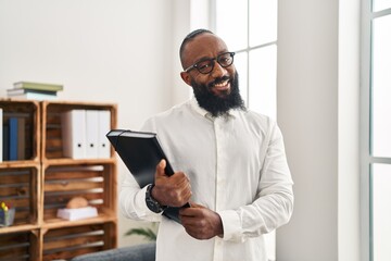 Young african american man psychologist holding binder at psychology center