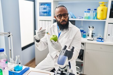 African american man working at scientist laboratory with apple puffing cheeks with funny face. mouth inflated with air, catching air.