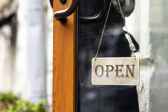 woman holds a wooden sign with the inscription open or closed at the door of a restaurant or coffee shop. the working hours of the restaurant or the food and beverage delivery service. to the courier - Powered by Adobe