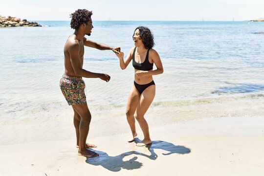 Young interracial tourist couple wearing swimwear dancing at the beach.
