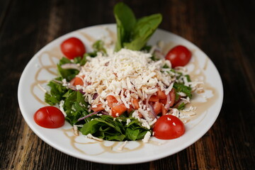 Salad mix with tomato, cucumber, olive oil, onion slices, and grated cheese in a bowl on a wooden table. Healthy food. Vegetarian food. 
