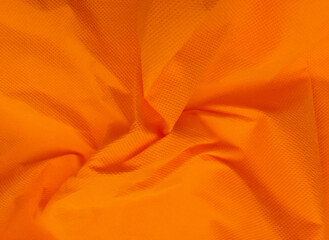 coarse porous orange color non-woven fabric surface background. wrinkled and chaotic polypropylene fabric texture