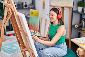 Young hispanic woman artist listening to music drawing at art studio