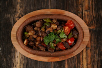 Saute meat in a stew on a wood background. Meat saute made with beef, mushroom, onion, green pepper and tomatoes. A delicious traditional Turkish food name is Guvec. Top view.