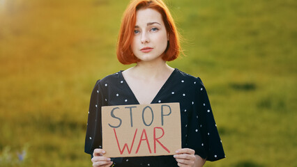 Unhappy caucasian young redhead woman activist hold demonstrating banner with inscription stop war...