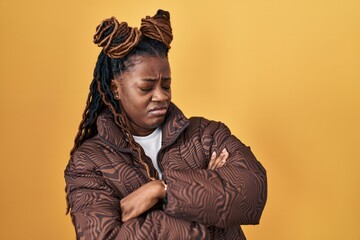African woman with braided hair standing over yellow background looking to the side with arms crossed convinced and confident