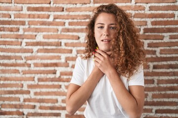 Young caucasian woman standing over bricks wall background shouting and suffocate because painful strangle. health problem. asphyxiate and suicide concept.
