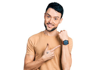 Hispanic man with beard wearing casual t shirt in hurry pointing to watch time, impatience, looking...