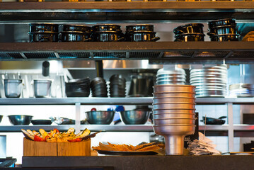 Modern shiny kitchen with stainless still kitchenware and equipment for restaurant-scale cooking with preparation tables, pans, pots, stoves.
