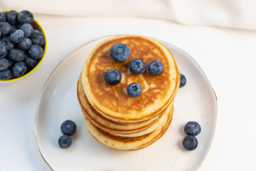 Stack of delicious pancakes on white plate with fresh blueberries on and in bowl. Top view, Copy space