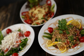 Different types of mixed salad with tomato, cucumber, olive oil, onion slices, and grated cheese in a bowl on a wooden table. Healthy food. Vegetarian food.  