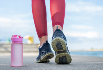 girl athlete runs in the morning in sneakers with a bottle of water
