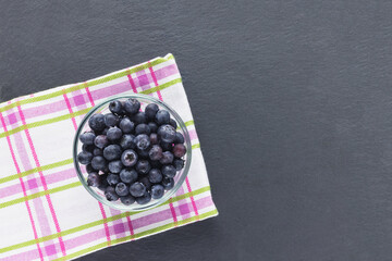 Blueberries in glass bowl on black background with kitchen cloth towel, concept of healthy eating vegan food and snack. Top view, copy space