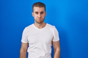 Fototapeta premium Young caucasian man standing over blue background depressed and worry for distress, crying angry and afraid. sad expression.