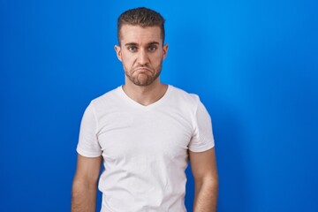 Young caucasian man standing over blue background depressed and worry for distress, crying angry and afraid. sad expression.