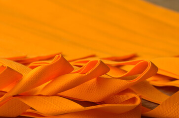 detail of the orange color non woven bag strap. selective focus. porous polypropylene tote bag stacks and folds