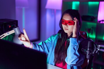 Young chinese woman streamer playing video game using virtual reality glasses at gaming room